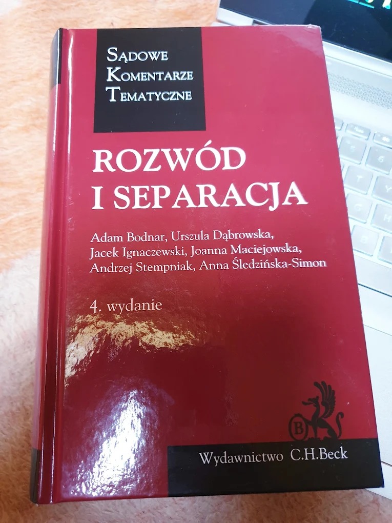 Czerwona książka 'Sądowe Komentarze Tematyczne: Rozwód i Separacja', czwarte wydanie, leżąca na biurku obok laptopa.