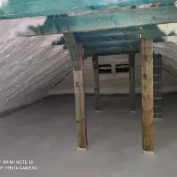 Poddasze ocieplone pianką PUR, widoczne drewniane elementy konstrukcyjne pomalowane na zielono i fragment okien dachowych.