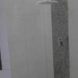 Wykończona kabina prysznicowa z deszczownicą i odpływem liniowym. Białe płytki imitujące marmur zestawione z mozaiką. Oświetlenie LED w suficie.