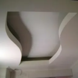 Dekoracyjny sufit podwieszany z płyt kartonowo-gipsowych z asymetrycznymi, falistymi wycięciami, oświetlony od góry, widok z dołu.