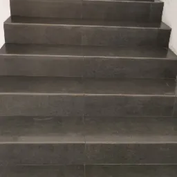 Wykończone schody z ciemnych, matowych płytek ceramicznych z widoczną białą fugą, na dole kadru leży kielnia do fugowania.