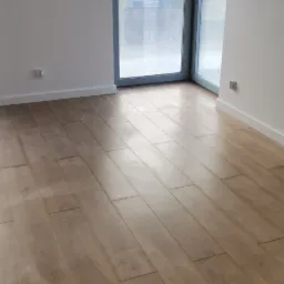 Nowo położona, jasna podłoga panelowa w pustym pokoju z dużym oknem balkonowym i białymi ścianami.