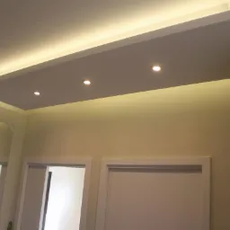 Podwieszany sufit z oświetleniem LED i punktowymi lampami, białe ściany, minimalistyczny design. Widoczne drzwi i lustro w tle.