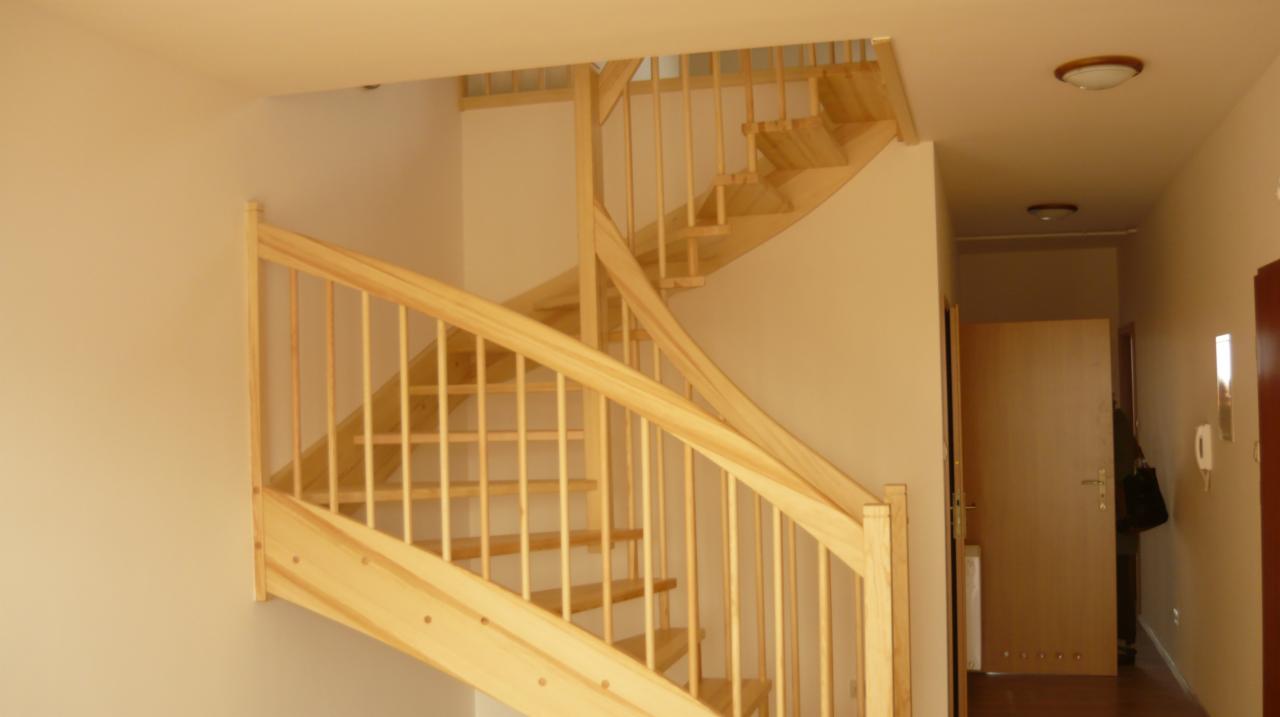 Jasne, drewniane schody kręte z balustradą w nowym domu, widok z dołu na górę, w tle korytarz z drzwiami.