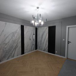 ERBUD ERNEST ŻABICKI - Nowoczesne wnętrze: parkiet w jodełkę, ściany z marmurowymi panelami i czarnymi wstawkami, designerski żyrandol. Minimalistyczny styl, szaro-biała kolorystyka.