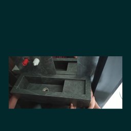 ERBUD ERNEST ŻABICKI - Wyjątkowa, kamienna umywalka w odcieniach szarości, z widocznymi elementami instalacji wodnej. Umywalka o geometrycznym kształcie, z wyraźną fakturą kamienia.