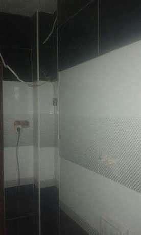 Nowoczesna łazienka z czarno-białymi płytkami, kabina prysznicowa ze szklaną ścianką i widoczną instalacją elektryczną przed wykończeniem.