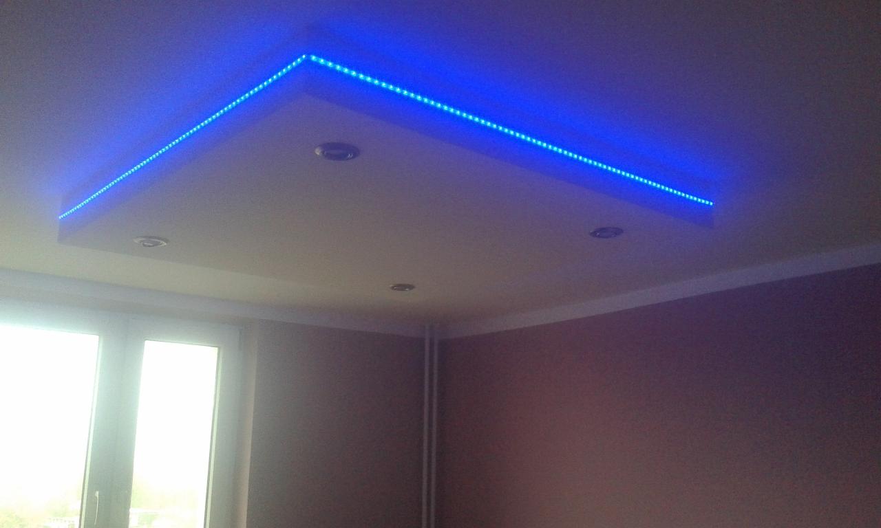 Podwieszany sufit z oświetleniem LED w kolorze niebieskim i wbudowanymi reflektorami, widok z dołu, ściany w kolorze brudnego różu, okno z białymi ramami.
