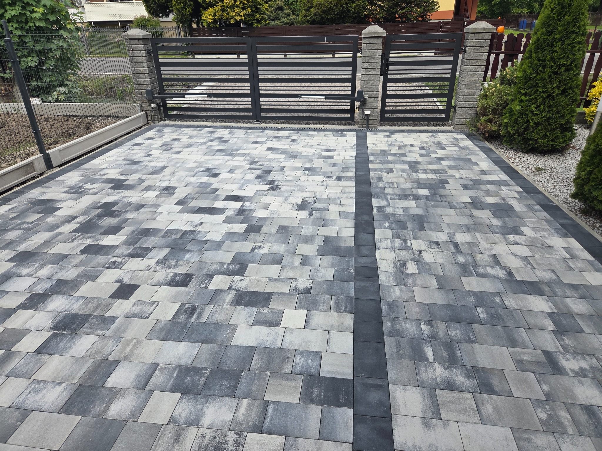 Ułożona kostka brukowa w odcieniach szarości, prowadząca do bramy w Drogomyślu. Widoczne geometryczne wzory i precyzyjne wykonanie.