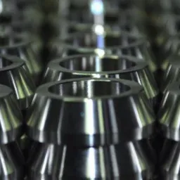 Rząd precyzyjnie wykonanych, metalowych elementów w kształcie ściętego stożka z otworem, ułożonych jeden na drugim. Powtarzalność detali i obróbka powierzchni.