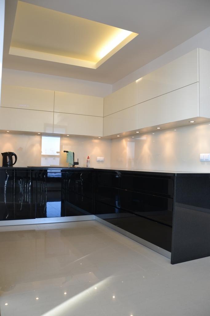 Nowoczesna kuchnia z czarnymi, lakierowanymi szafkami dolnymi i jasnymi górnymi, podświetlana listwami LED, z błyszczącą podłogą.