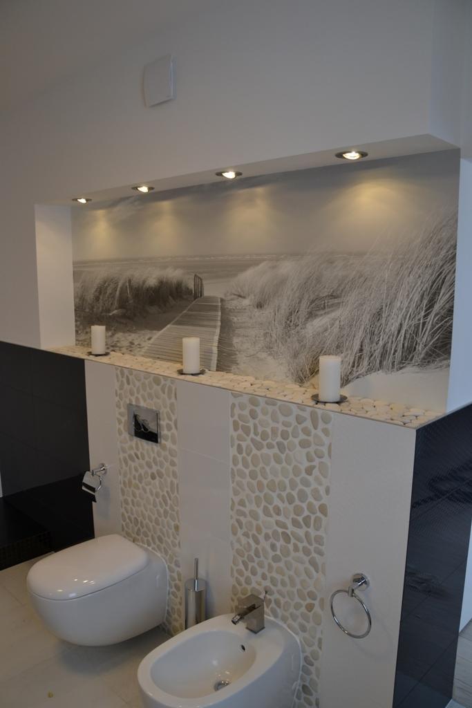 Nowoczesna łazienka z fototapetą plaży i białymi kamieniami, toaleta podwieszana i bidet. Dekoracyjne oświetlenie punktowe.