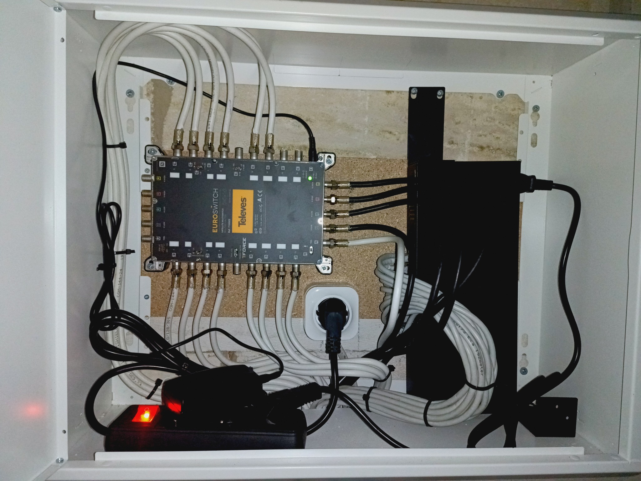 Rozdzielacz sygnału TV w białej szafce, liczne kable antenowe i zasilające. Widoczny model Televes Euroswitch. Instalacja wewnątrz obudowy.