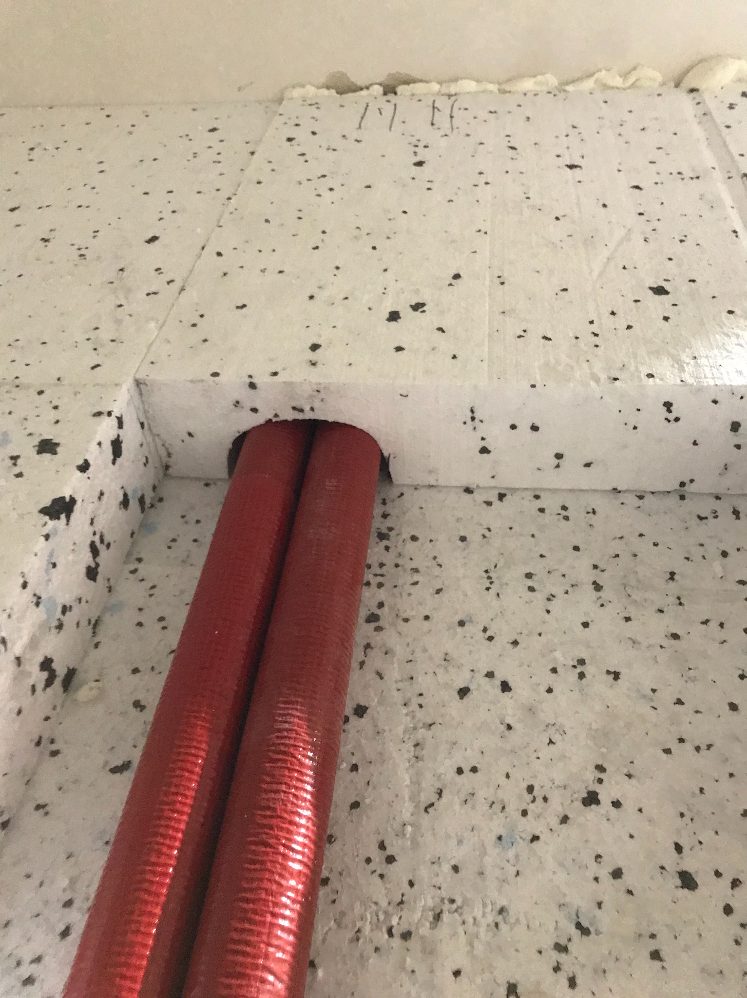 Dwa czerwone rury grzewcze w izolacji podłogowej z polistyrenu, widoczne z dołu.