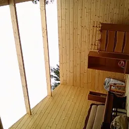 Wnętrze altany z drewnianą boazerią, widok na niebo przez przeszklony dach, częściowo umeblowane, w trakcie prac wykończeniowych.