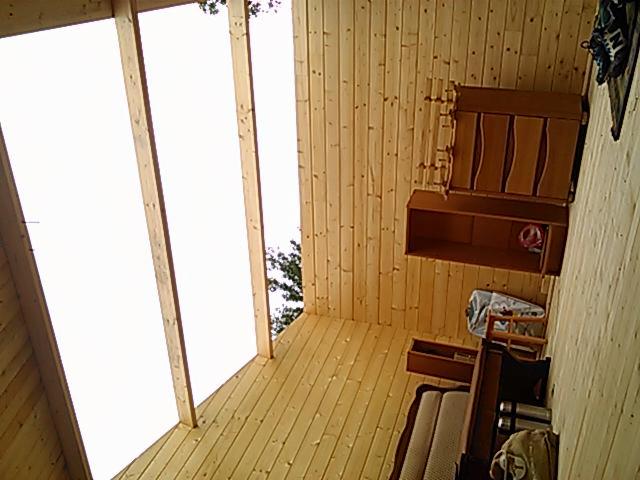 Wnętrze altany z drewnianą boazerią, widok na niebo przez przeszklony dach, częściowo umeblowane, w trakcie prac wykończeniowych.