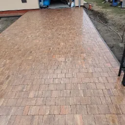 Nowa, brązowo-czerwona kostka brukowa ułożona na podjeździe przed garażem, widok z góry na całą powierzchnię, detale faktury poszczególnych kostek.