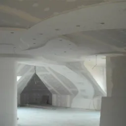 Kreatywna zabudowa poddasza z płyt gipsowo-kartonowych. Wykończony sufit z wbudowanym oświetleniem punktowym i dekoracyjnymi elementami. Widoczne łączenia płyt wymagające szpachlowania.