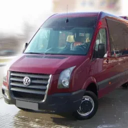 Czerwony bus Volkswagen Crafter z czarnymi felgami na parkingu, widok z przodu i boku, światło odbija się od mokrej nawierzchni.