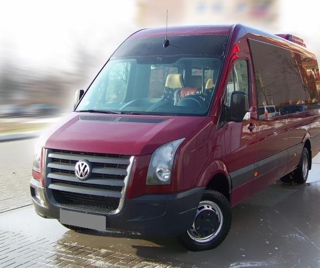 Czerwony bus Volkswagen Crafter z czarnymi felgami na parkingu, widok z przodu i boku, światło odbija się od mokrej nawierzchni.