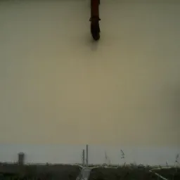 Ściana budynku po tynkowaniu, z widoczną rurą spustową i fragmentem rusztowania, dolna część ściany pomalowana na biało, trawa przy podstawie.