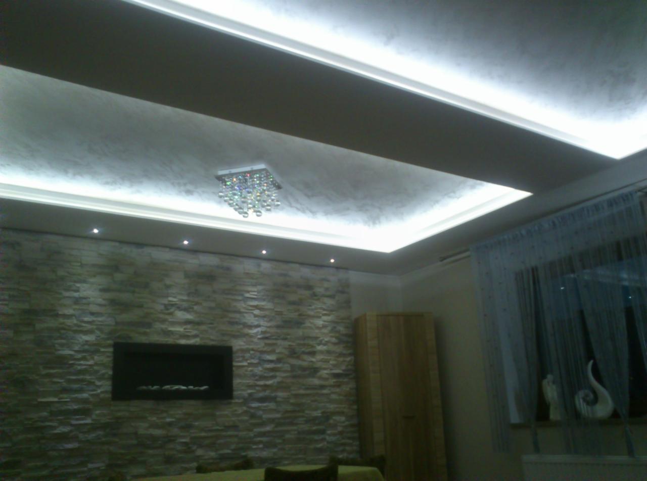 Nowoczesne wnętrze z podwieszanym sufitem z oświetleniem LED, dekoracyjną ścianą z kamienia, elektrycznym kominkiem i kryształowym żyrandolem