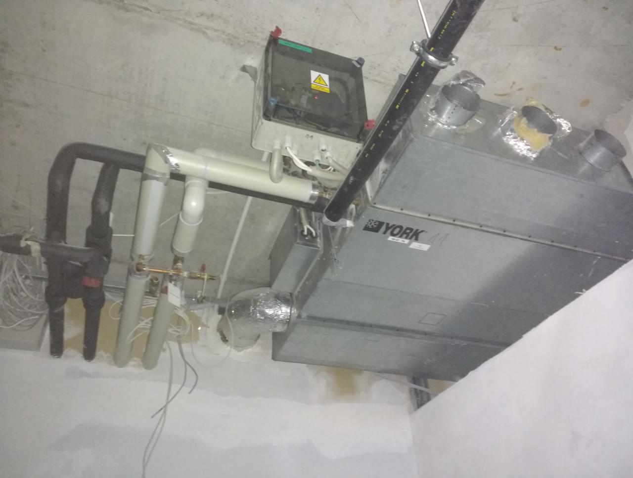 Widok instalacji rekuperacji w surowym stanie, widoczne rury, centrala rekuperacyjna marki York oraz przewody elektryczne.