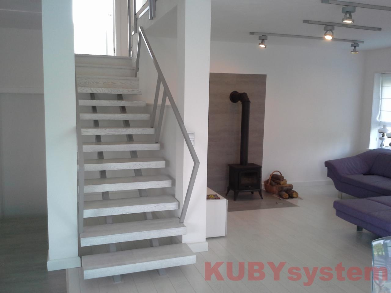 Nowoczesne schody drewniane o jasnych stopniach i metalowej balustradzie, umieszczone w jasnym wnętrzu z kominkiem i fioletową sofą. Minimalistyczny design.