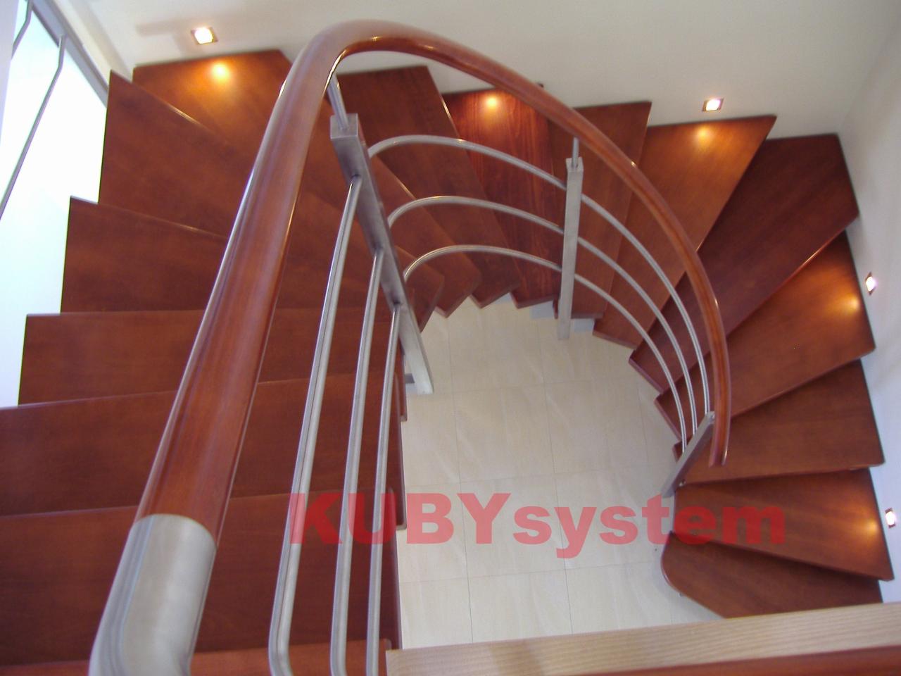 Spiralne schody z drewnianymi stopniami i metalową balustradą, widok z góry, oświetlone punktowo, z delikatnym logo na dolnym biegu.