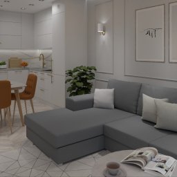 PMP KONKRET SPÓŁKA Z OGRANICZONĄ ODPOWIEDZIALNOŚCIĄ - Wnętrze kawalerki: szara sofa narożna, stół z pomarańczowymi krzesłami i aneks kuchenny w bieli. Na ścianie grafiki w ramkach, parkiet w jodełkę.