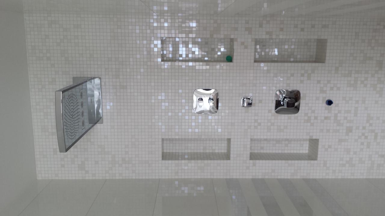 Nowoczesna kabina prysznicowa z armaturą w kształcie kwadratu i mozaiką w odcieniach bieli. Widoczne wnęki w ścianie i deszczownica.