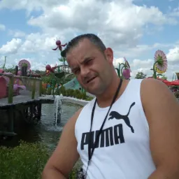 Mężczyzna w parku rozrywki, na tle dekoracji kwiatowych i fontanny, w słoneczny dzień.