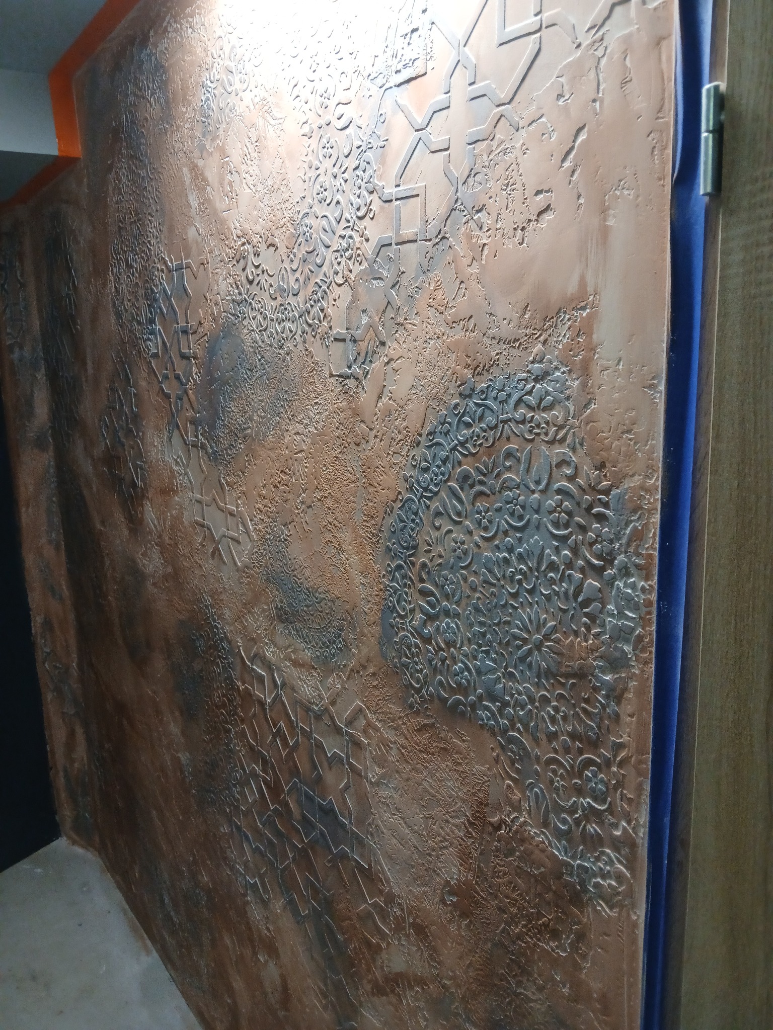 Dekoracyjna ściana z unikalną fakturą i wzorami geometrycznymi oraz kwiatowymi w odcieniach brązu i szarości. Efektowna aranżacja wnętrza z bliska.