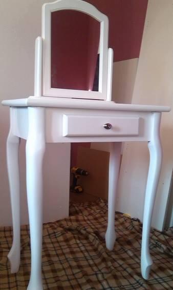 Biała toaletka z lustrem i szufladą, widoczna w całości, z detalami nóg i blatu. W tle widać wiertarkę, co sugeruje etap montażu lub renowacji.