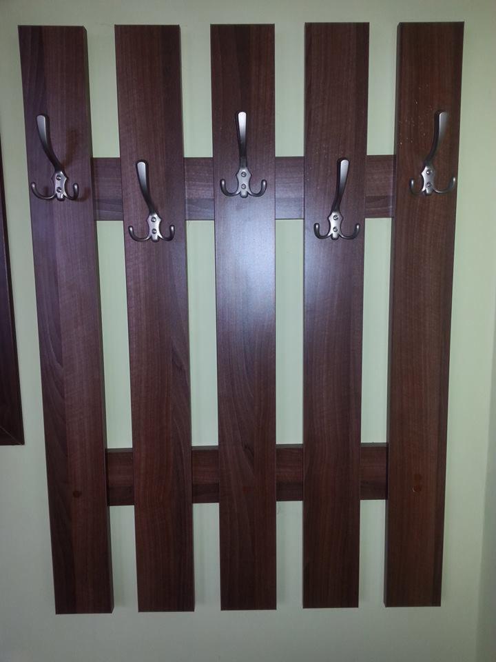 Wieszak ścienny z ciemnego drewna z pięcioma metalowymi haczykami, zamontowany na jasnej ścianie. Widoczne detale łączeń elementów drewnianych.