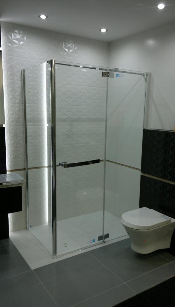 Nowoczesna kabina prysznicowa z chromowanymi profilami i szklanymi drzwiami, białe płytki 3D na ścianach, szara podłoga, minimalistyczny design.