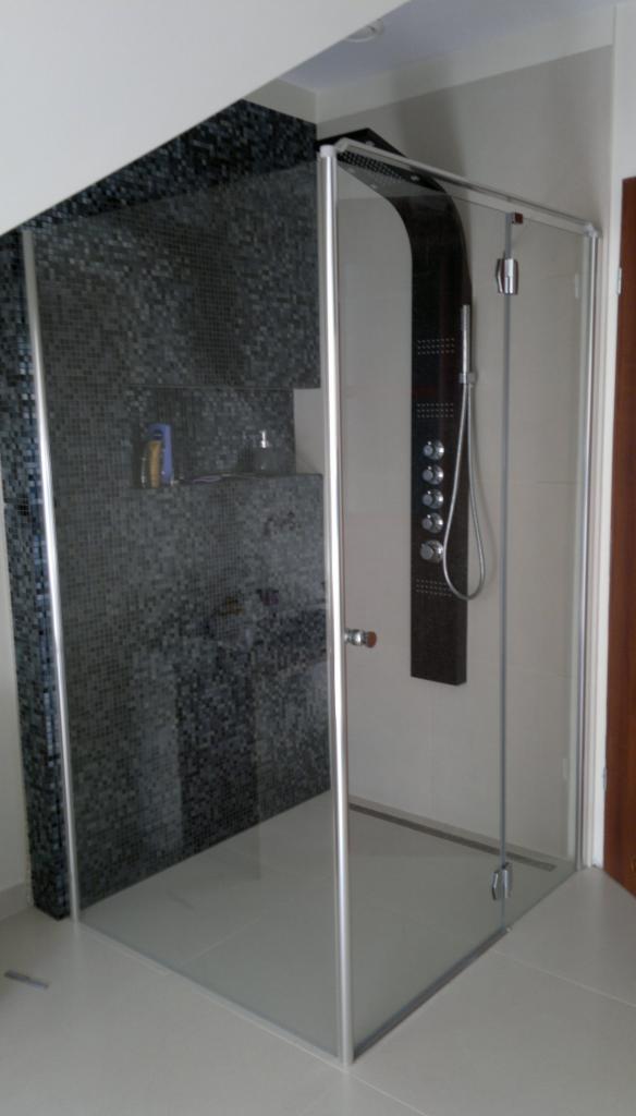 Nowoczesna kabina prysznicowa z czarną mozaiką i panelem natryskowym, wykończona w jasnych płytkach. Widoczne detale armatury i szklane drzwi.