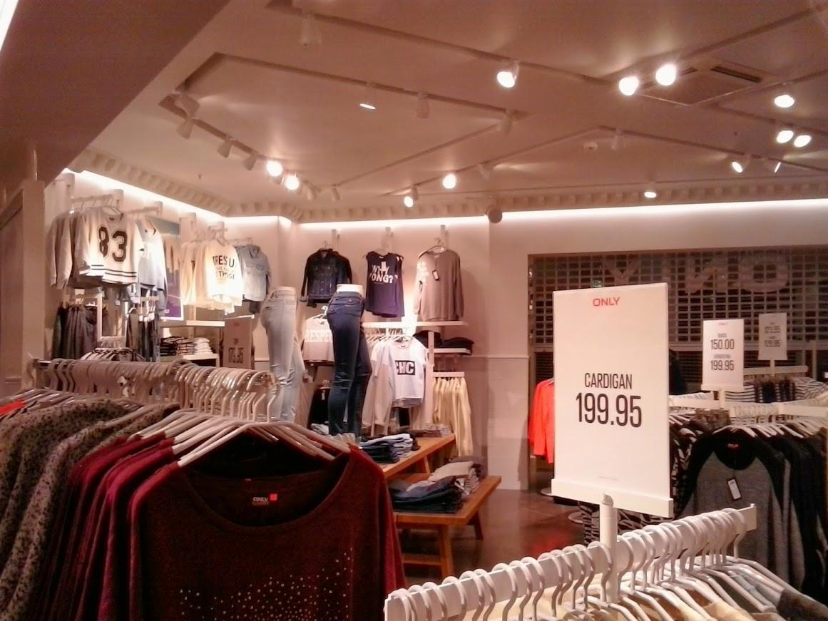 Wnętrze sklepu odzieżowego ONLY z różnorodnym asortymentem ubrań na wieszakach i półkach, oświetlone ciepłym światłem halogenów.