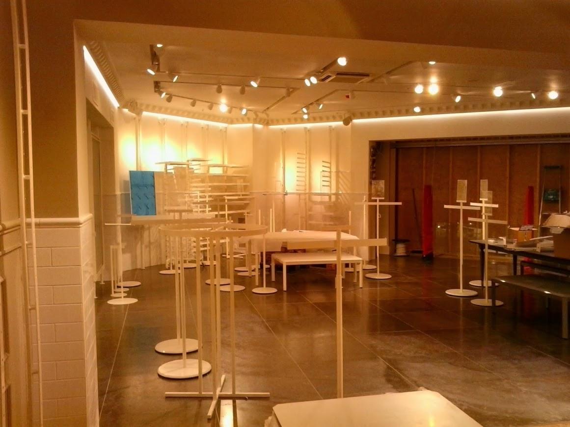 Jasne wnętrze sklepu odzieżowego w trakcie aranżacji: białe meble, oświetlenie punktowe, błyszcząca podłoga, widoczne elementy konstrukcyjne i przygotowania do ekspozycji.