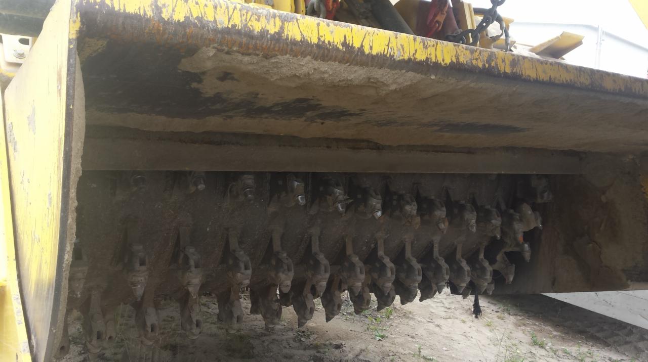 Żółty frez do pni z licznymi zębami tnącymi, widok od dołu, na ziemi. Narzędzie do karczowania pni drzew, gotowe do pracy.