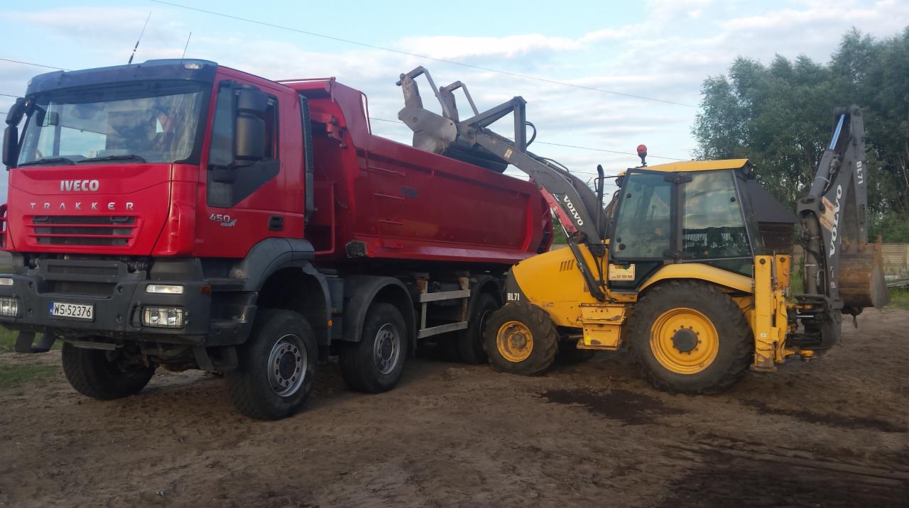 Czerwona ciężarówka Iveco Trakker i żółta koparko-ładowarka Volvo BL71 na placu budowy, sprzęt gotowy do pracy.
