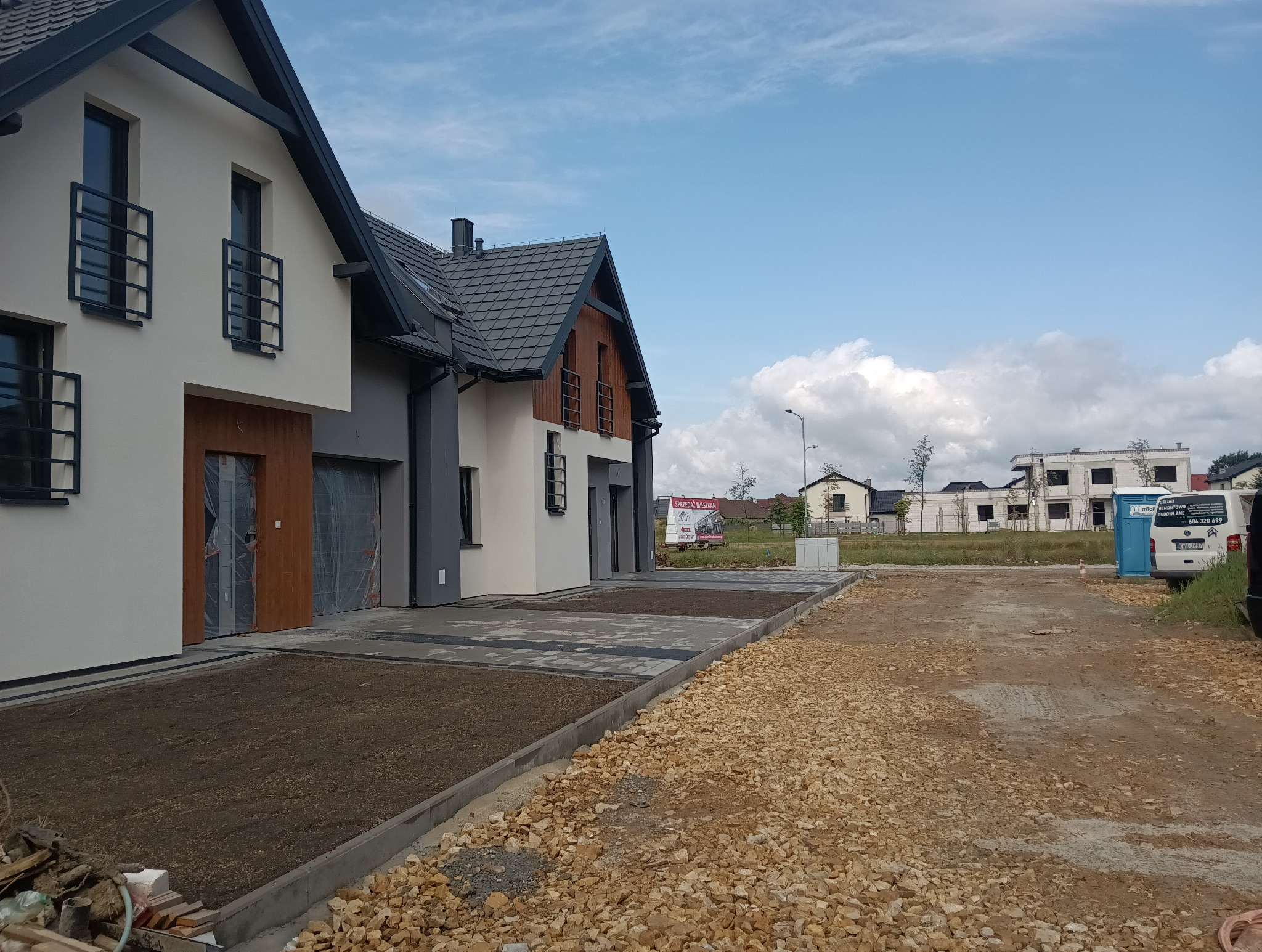 Nowoczesne domy w zabudowie szeregowej w Brzeszczach, z wykończonymi podjazdami i częściowo zagospodarowanym terenem, widok w słoneczny dzień.