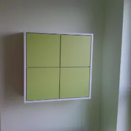 P&oacute;łka ścienna z czterema zielonymi frontami w białej ramie, zamontowana na jasnej ścianie. Widoczny fragment pokoju dziecięcego z boku.