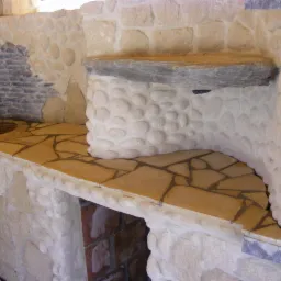 Kamienna zabudowa z blatem z nieregularnych płyt, zlew z kranem i półką z kamienia. Dekoracyjne wykończenie ścian z kamieni różnej wielkości i faktury.