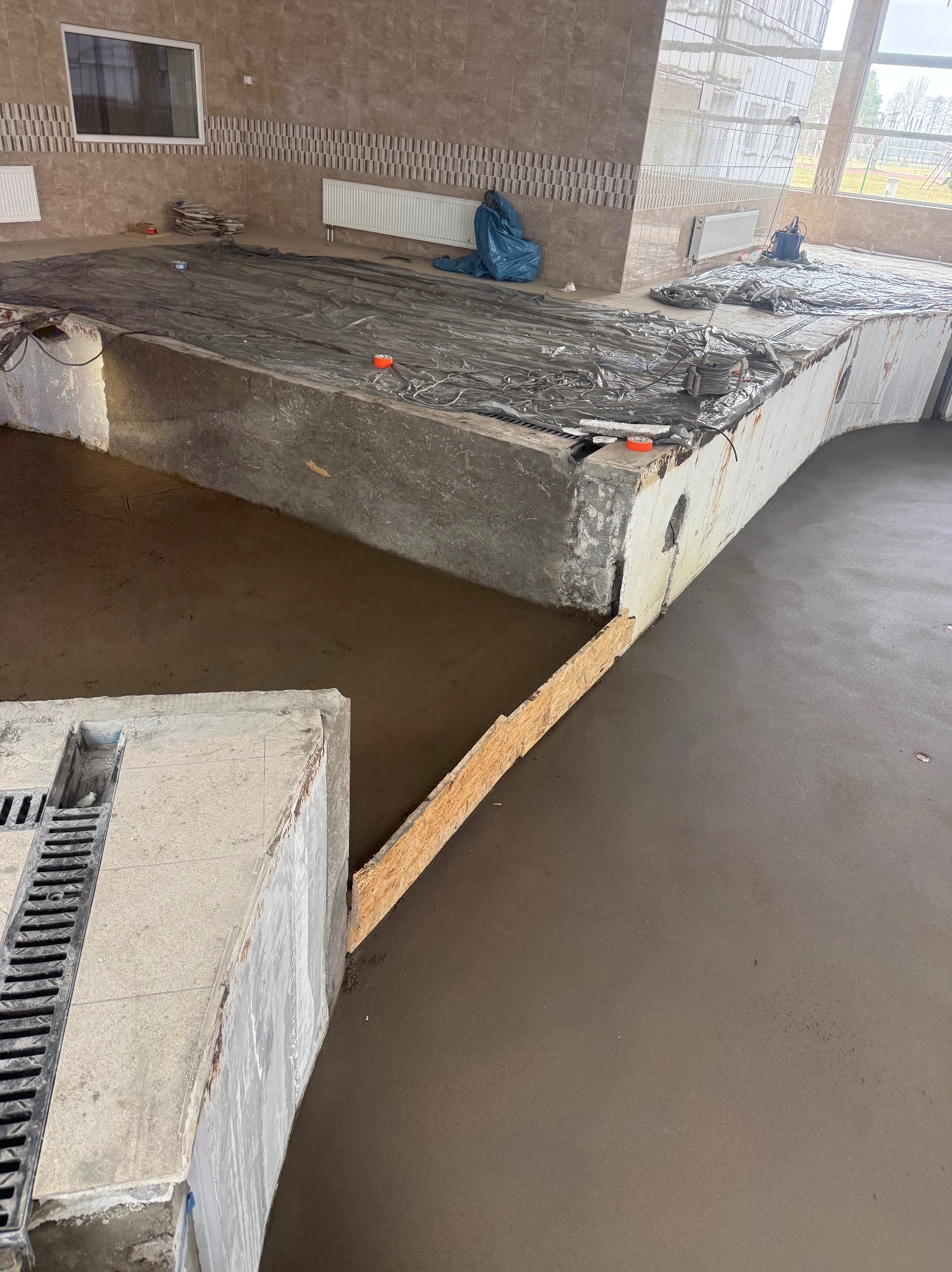 Wylewka samopoziomująca w Pieczyskach. Widoczny fragment posadzki z odpływem liniowym, zabezpieczone folią elementy i świeżo wylana, gładka powierzchnia.