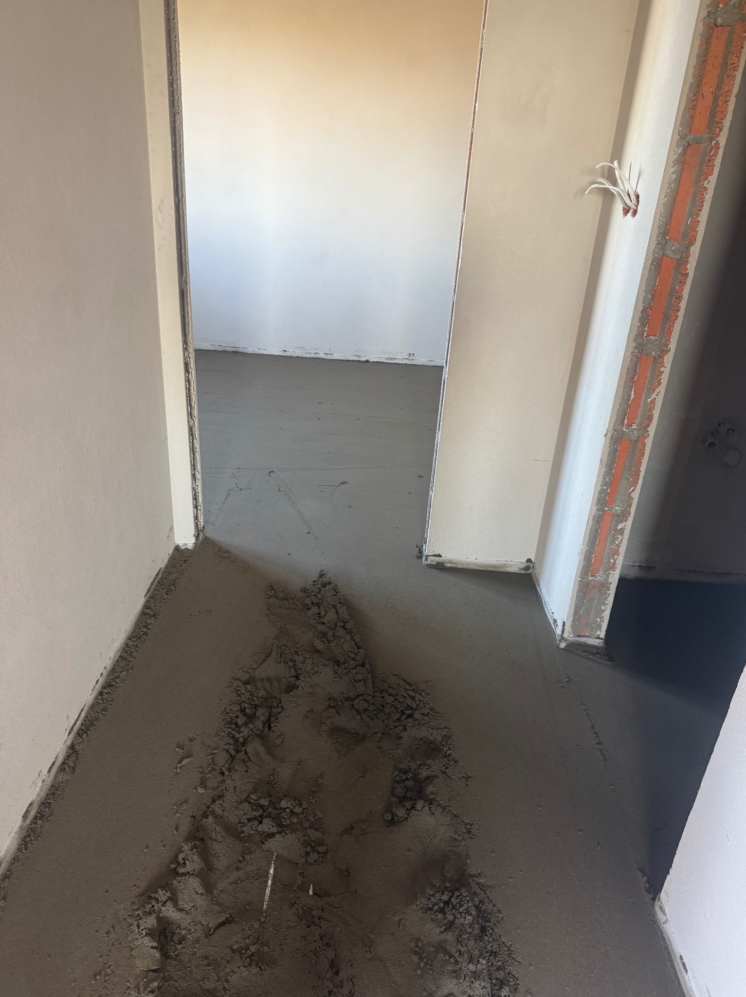 Wylewka podłogowa w trakcie realizacji, widoczne świeże zaprawy przy ścianach i w przejściach między pomieszczeniami. Surowy stan wykończenia wnętrza.