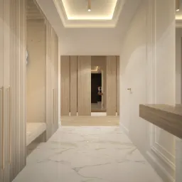 Korytarz w jasnych barwach z marmurową podłogą i zabudową meblową z ryflowanymi frontami. W głębi drewniane drzwi i oświetlenie sufitowe.