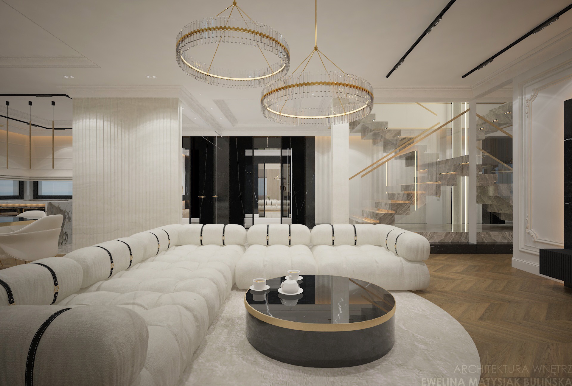 Elegancki salon w jasnych barwach z dużym, modułowym narożnikiem, okrągłym stolikiem kawowym i schodami z marmurowymi stopniami. Dwa okrągłe żyrandole z kryształkami.