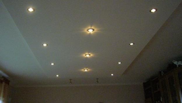 Podwieszany sufit z płyt karton-gips z zamontowanymi punktowymi lampami halogenowymi, oświetlającymi wnętrze. Widoczny fragment ściany i mebli.