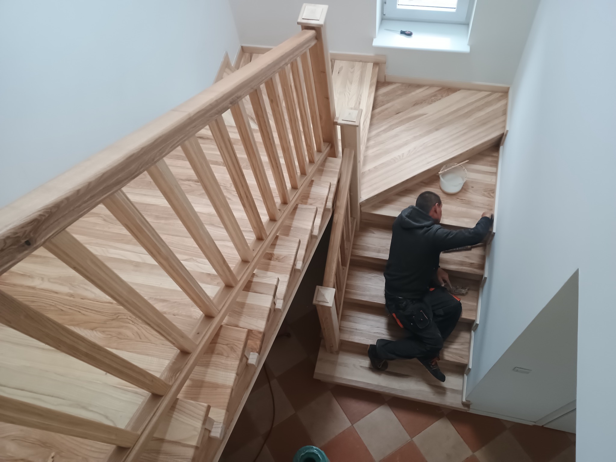 Montaż drewnianych schodów z balustradą przez stolarza. Widok z góry na jasne drewno i pracownika w trakcie wykończenia.